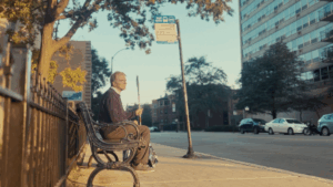 A man who is blind is seated at a bus stop.